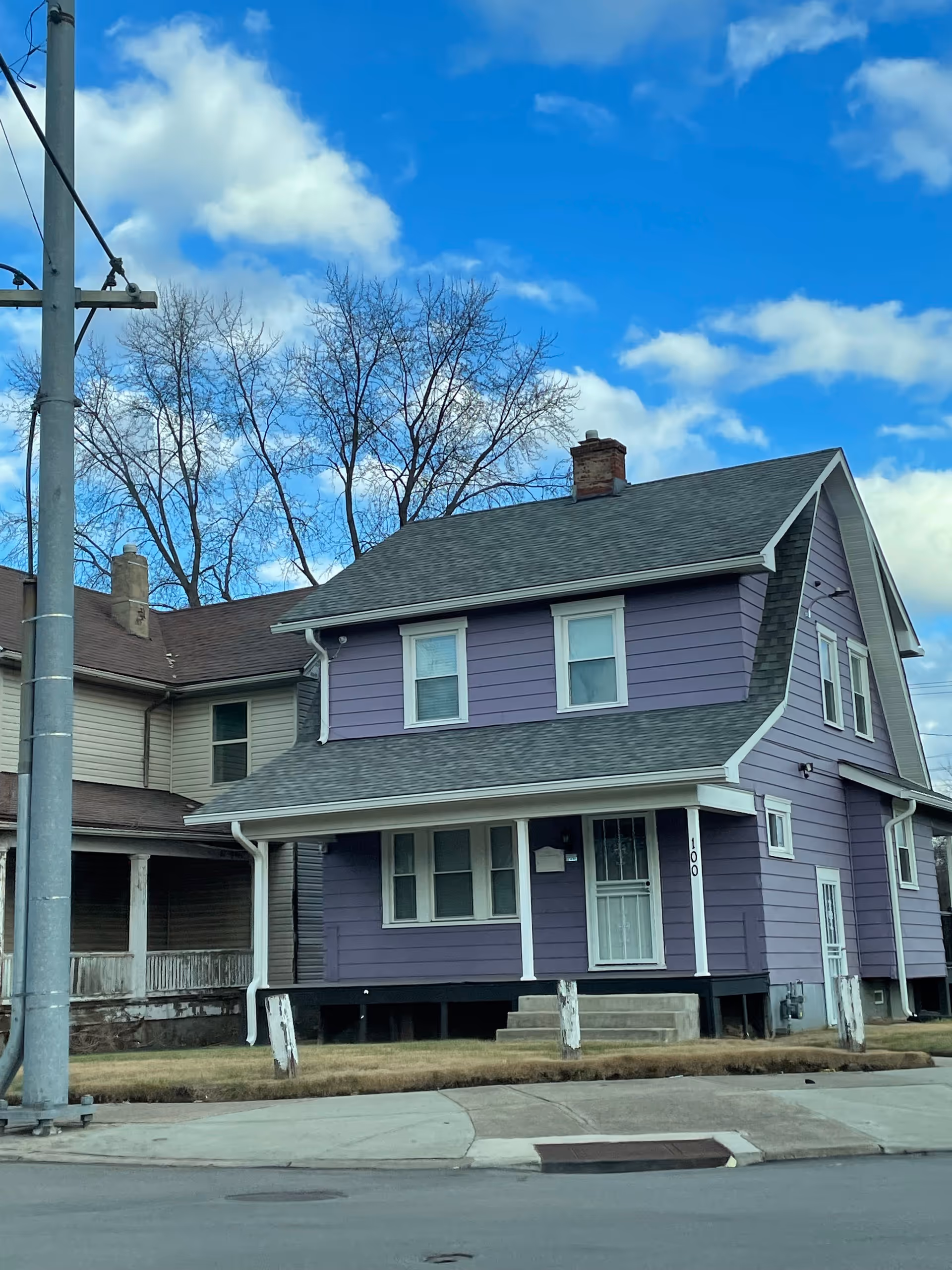 Two-story purple house with white trim on a street, blue sky and bare trees behind.