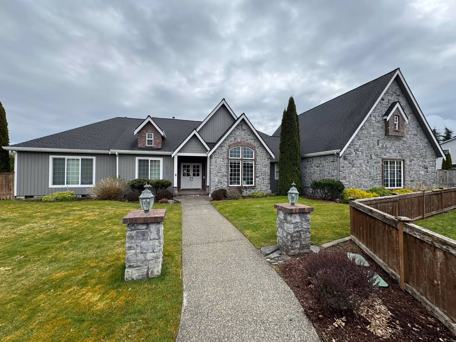 Front exterior of a gray stone-and-siding adult family home with a curved walkway to the entrance.