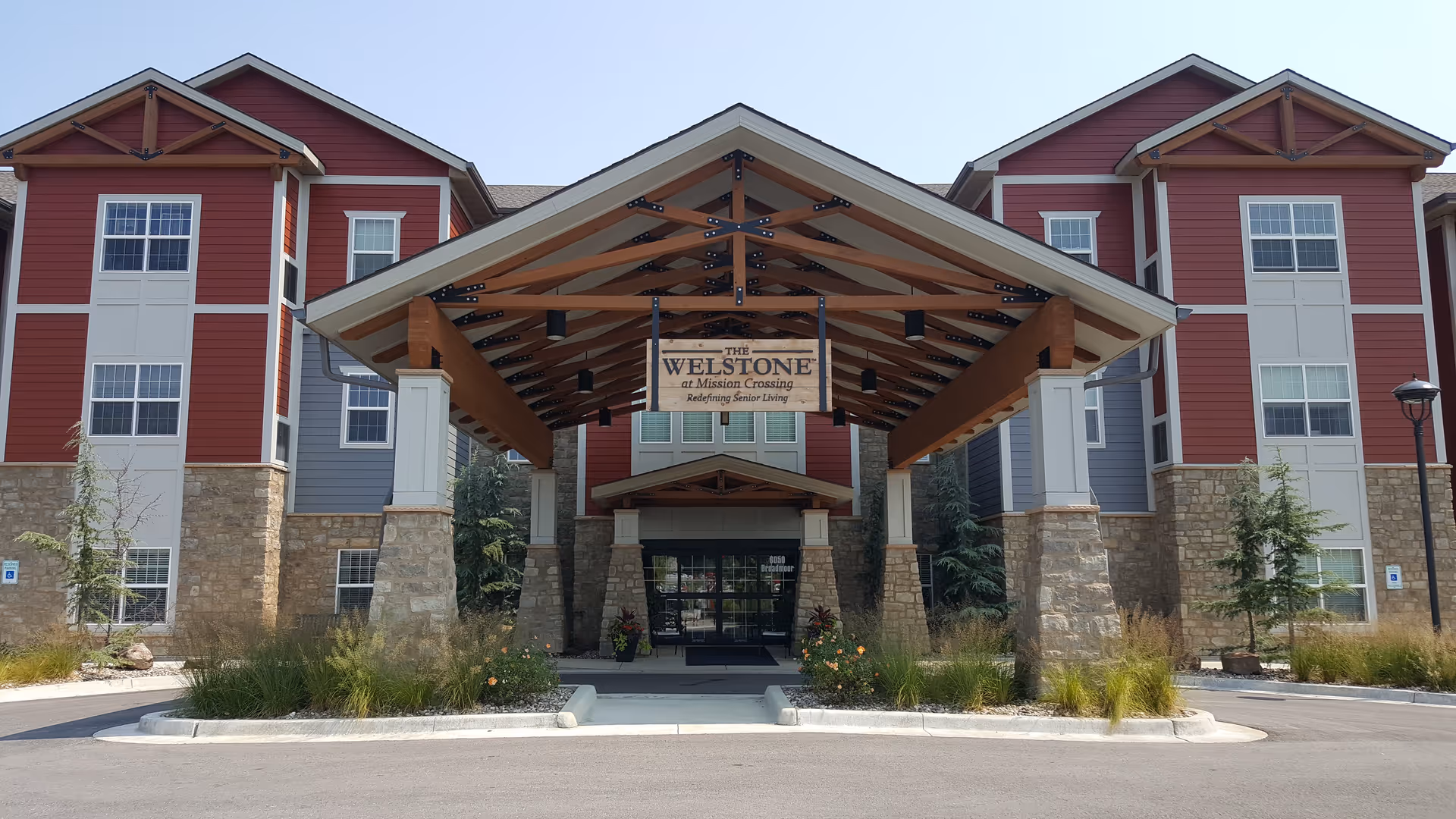Red and gray senior living building with a large wooden entry canopy and stone columns.