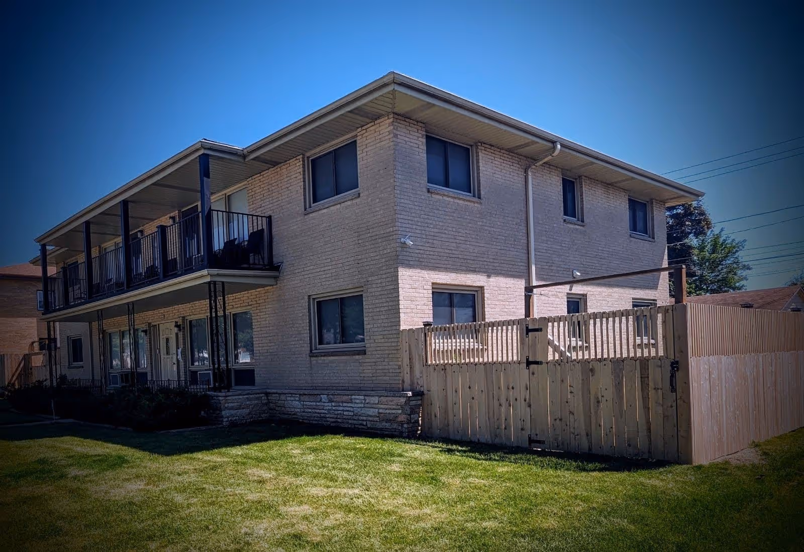Two-story brick senior living facility with balconies and a wooden privacy fence.