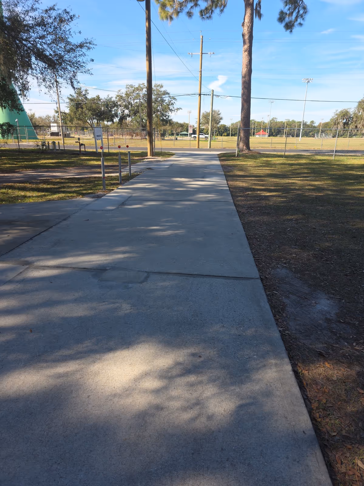 Sunny concrete walkway through outdoor facility grounds with trees and a fence.