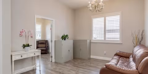 A bright living room in a senior care facility with a brown leather sofa and chandelier.