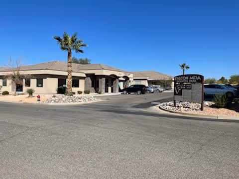 Single-story beige building with palm trees and a sign at the entrance.