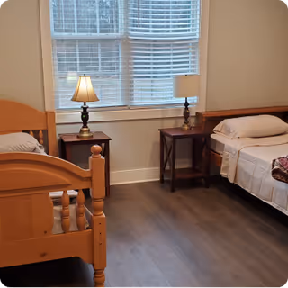 Two single beds with wooden frames flank a windowed wall in a shared bedroom.