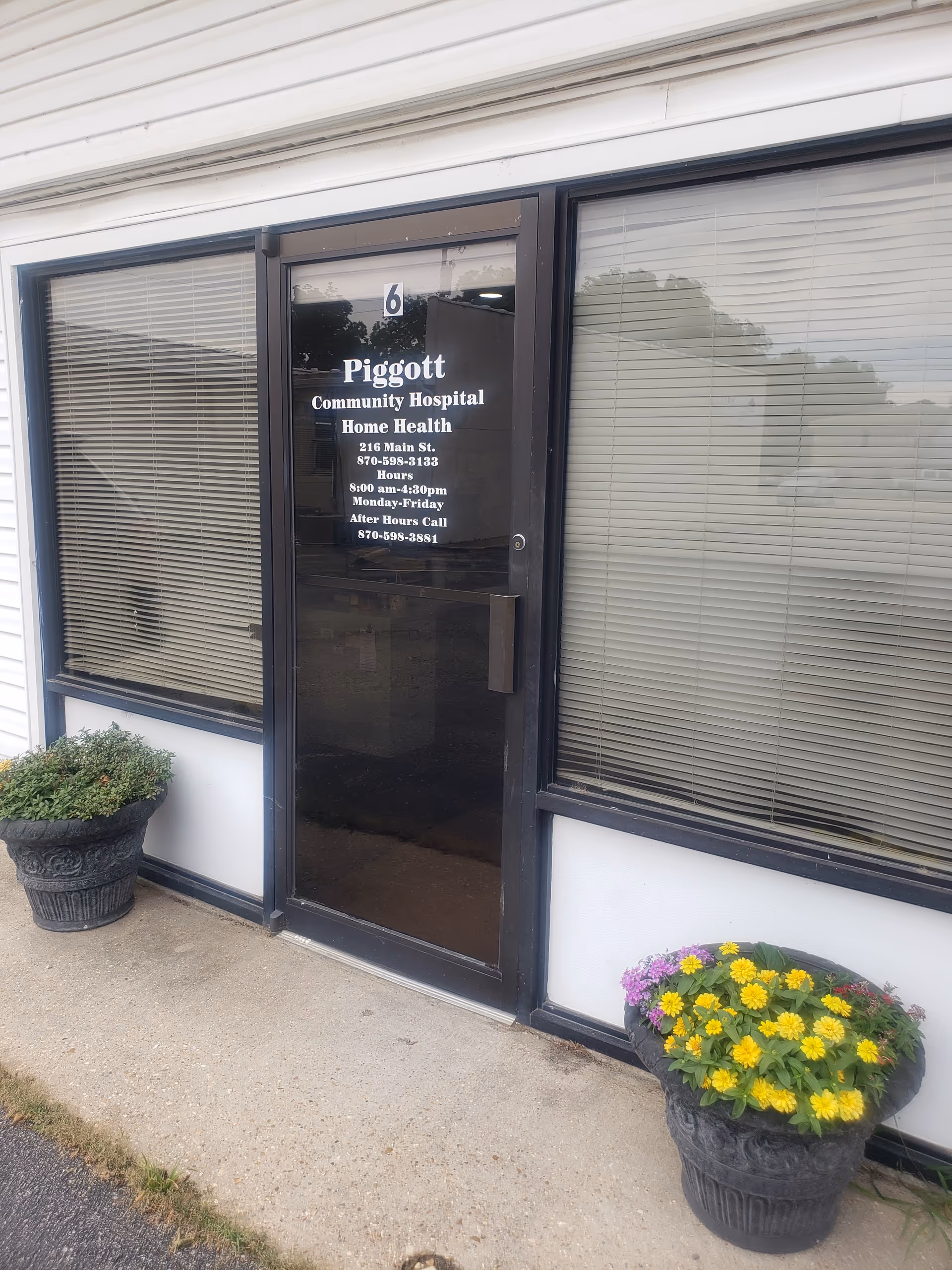 Front entrance of Piggott Community Hospital Home Health with glass door and potted plants.