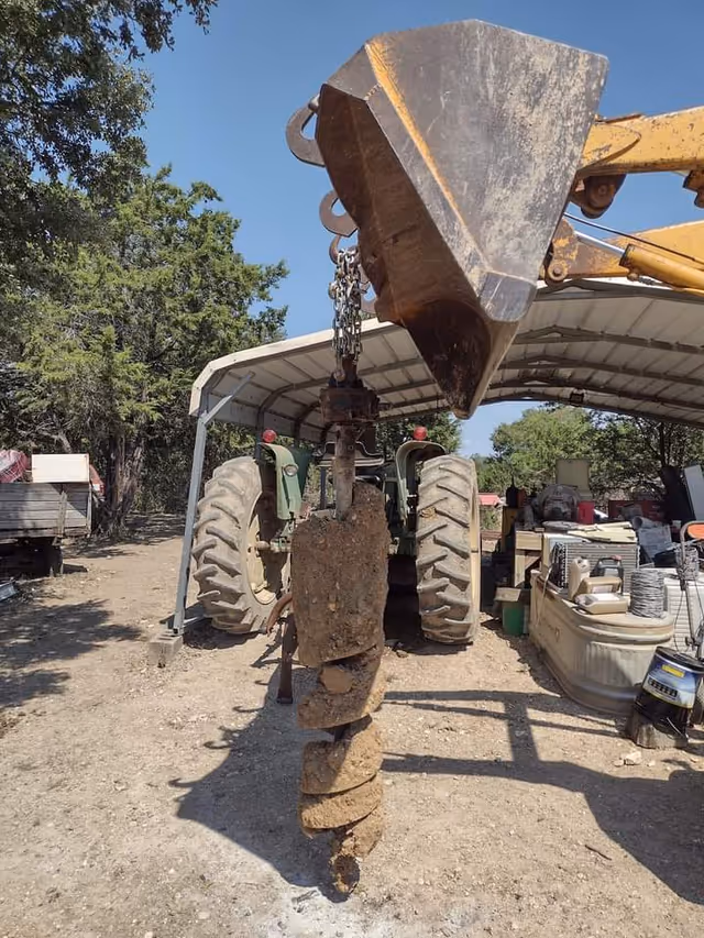 Construction yard with a large auger attached to a tractor beneath a metal shed.