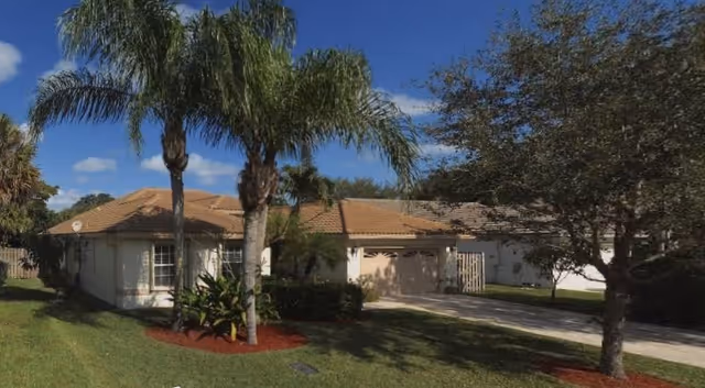 Single-story assisted living home with a front yard, palm trees, and a driveway.