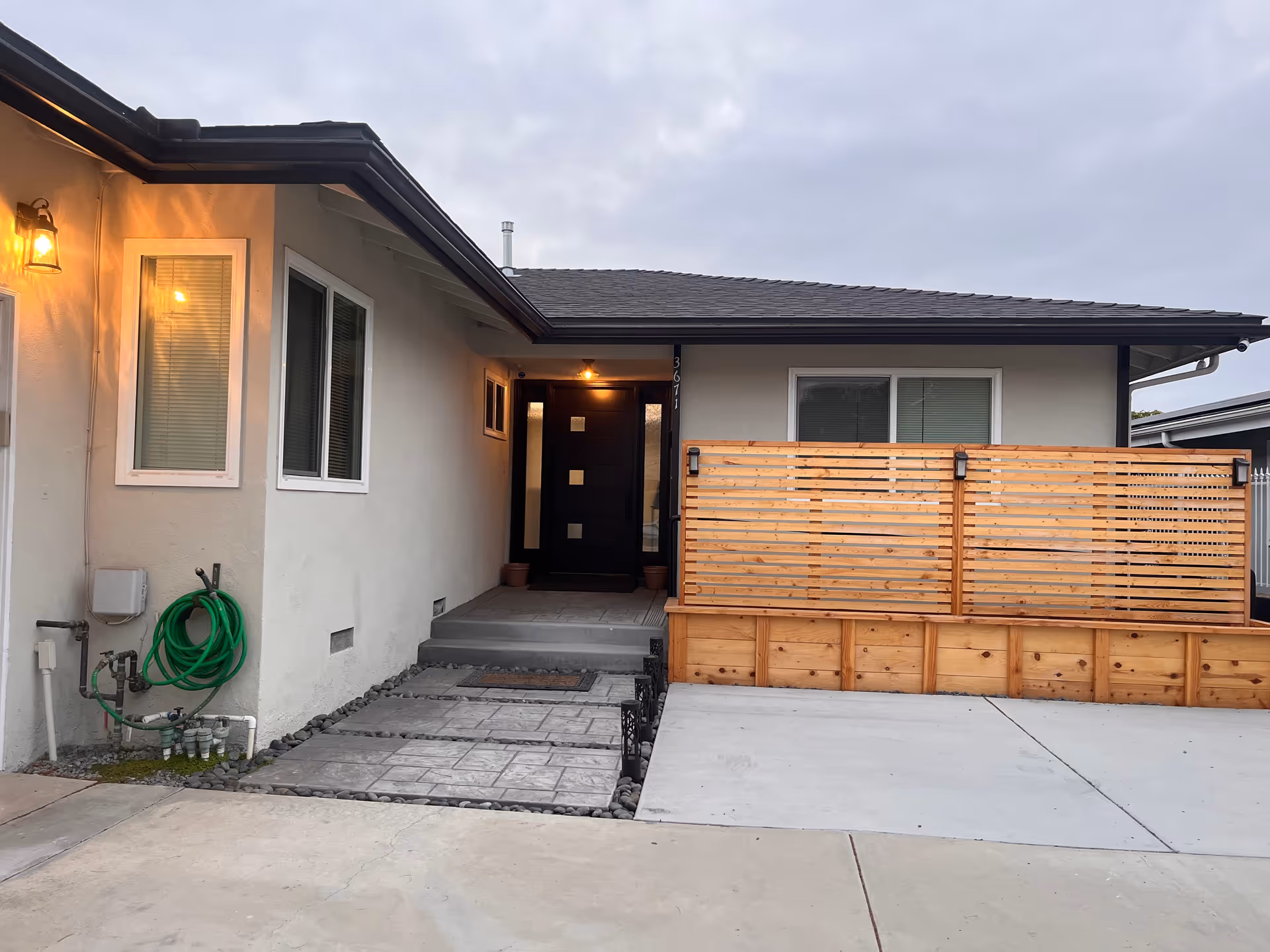 Residential-style single-story building with front entrance, wooden fence, and exterior hose by the wall.