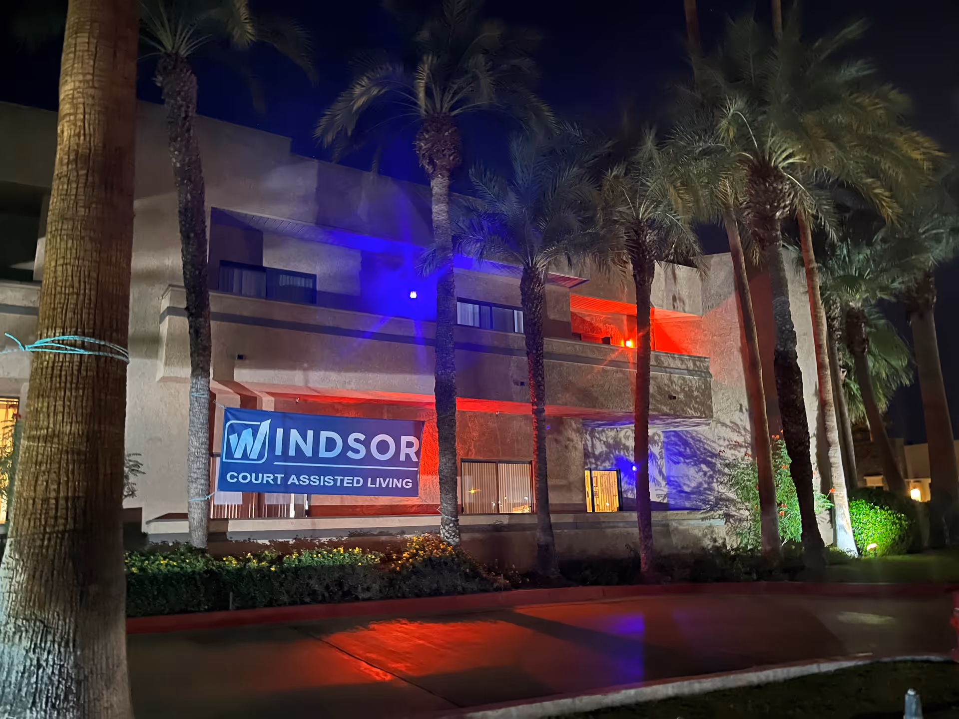 Windsor Court Assisted Living exterior at night with palm trees and a building banner.
