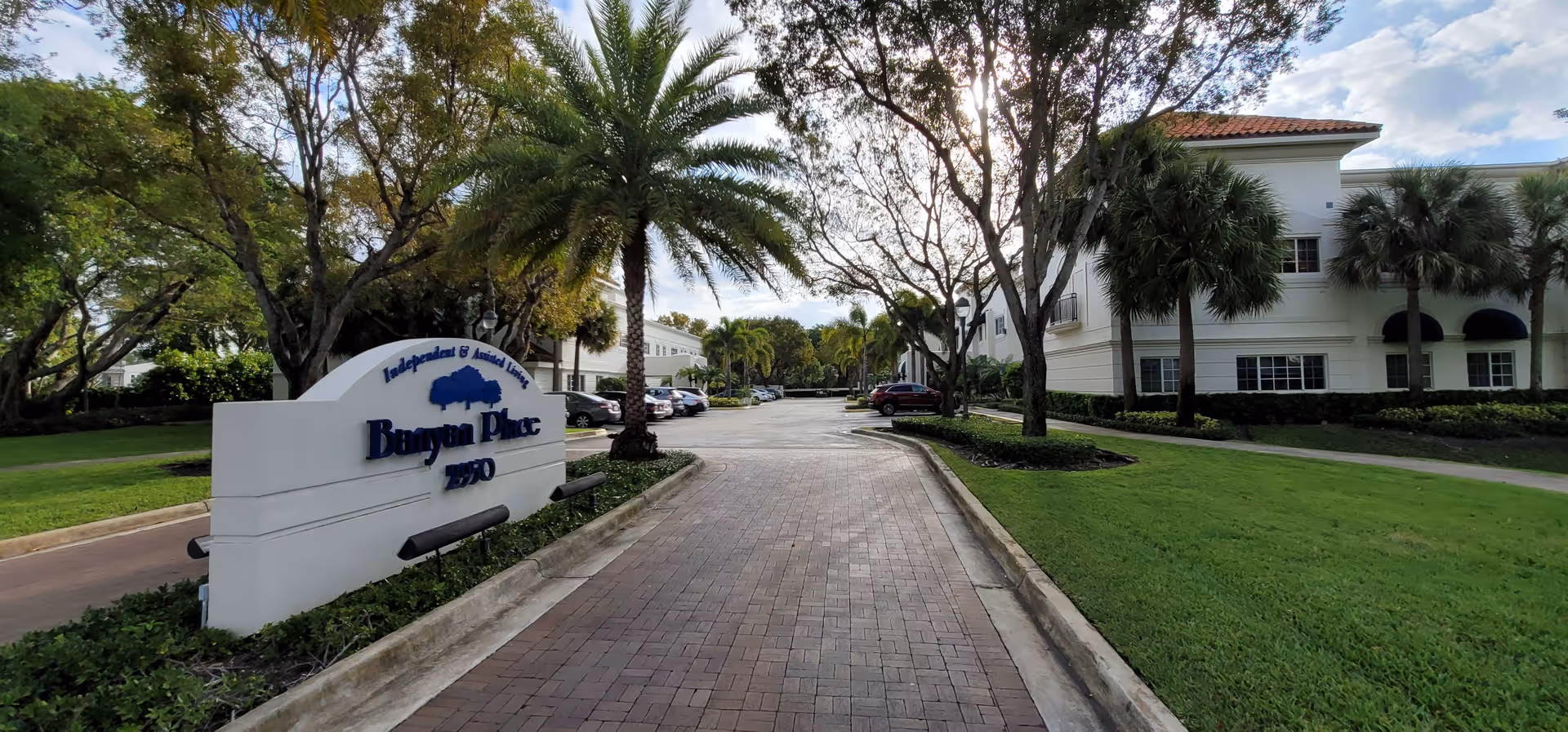 Exterior view of Banyan Place Boca Raton with brick walkway, sign, and palm trees.