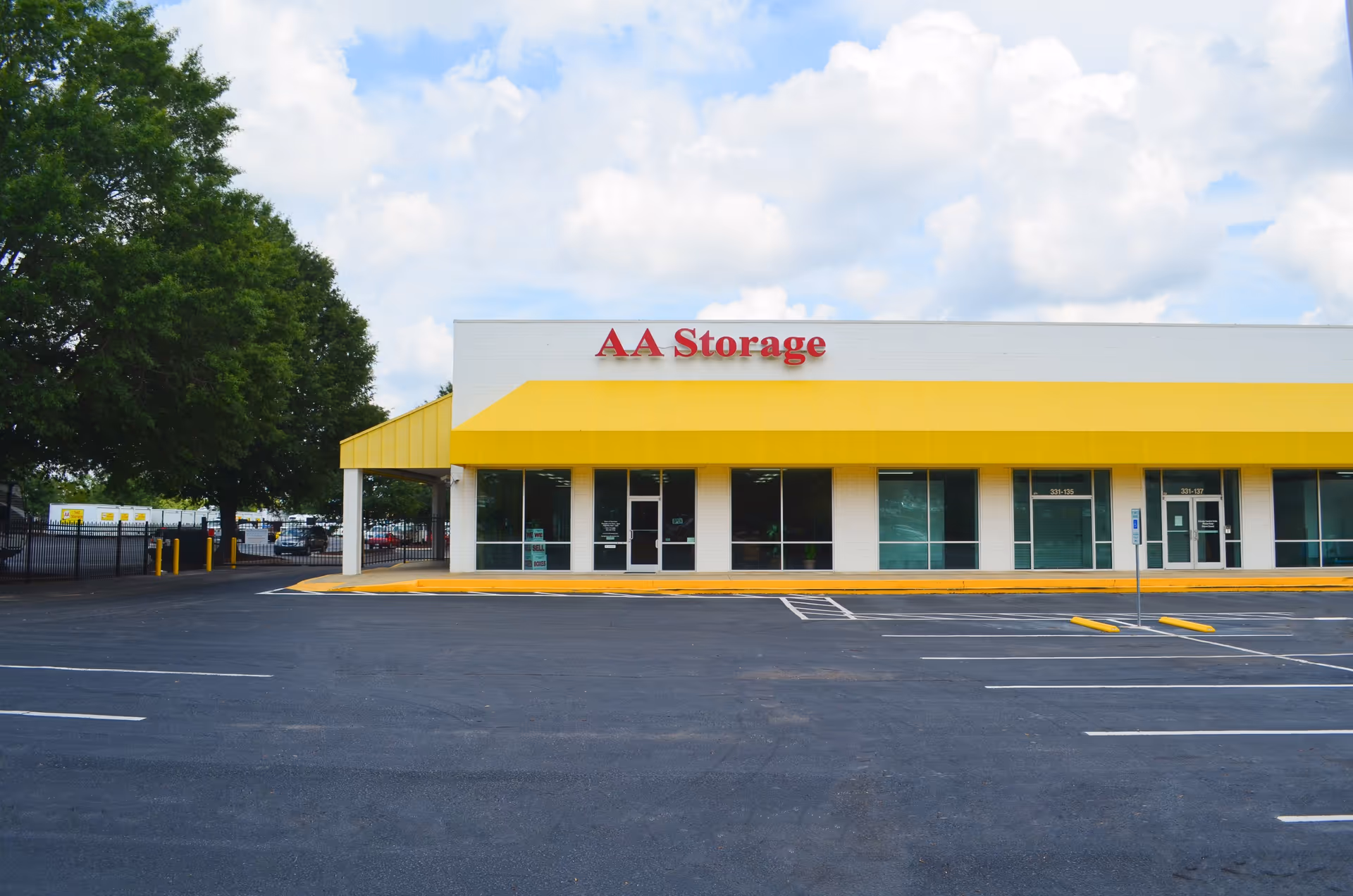 A single-story storefront with a bright yellow awning labeled AA Storage and a large parking lot.