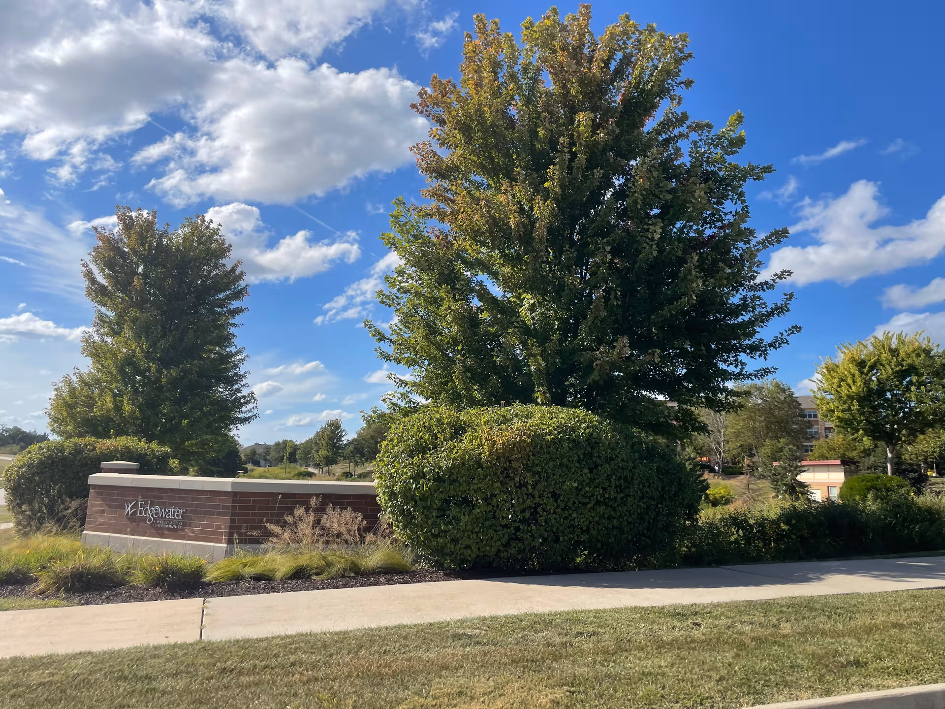 Exterior view of Edgewater facility with a brick sign and green trees under blue sky.