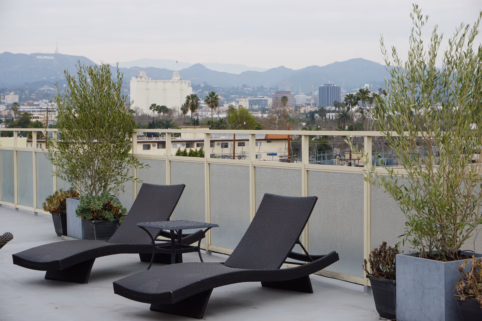 Two black wicker lounge chairs and a small table on a rooftop terrace with potted plants.