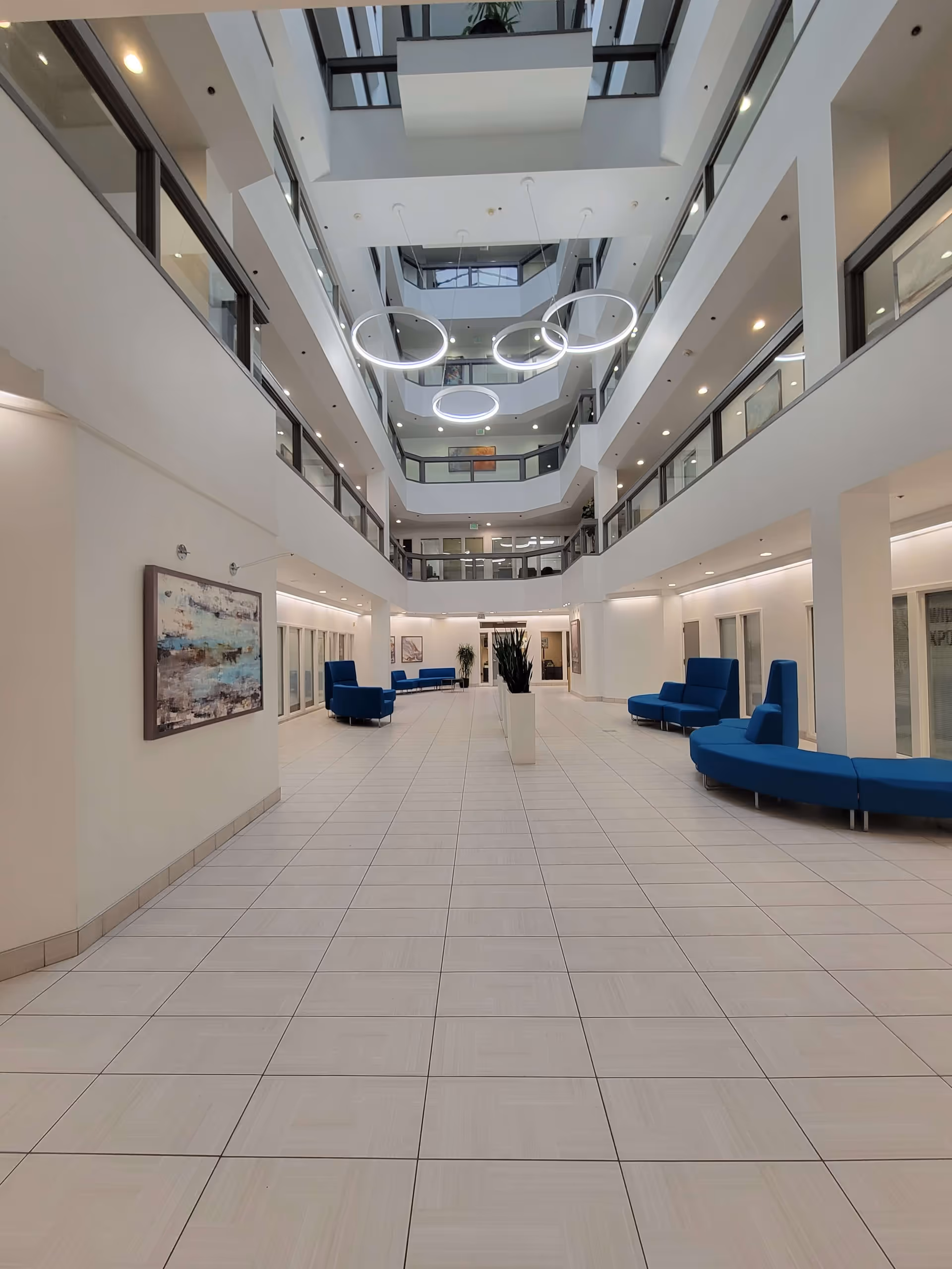 Bright, multi-level atrium with circular ring lights, white walls, and blue lounge seating.