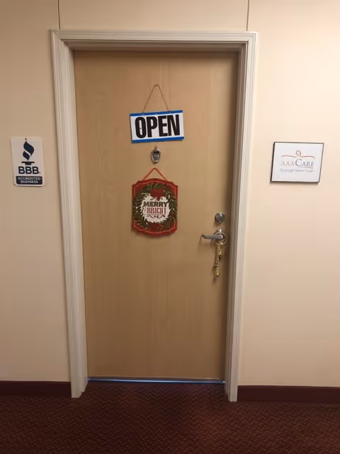 Interior hallway with a wooden door marked OPEN, holiday wreath, and facility signs.