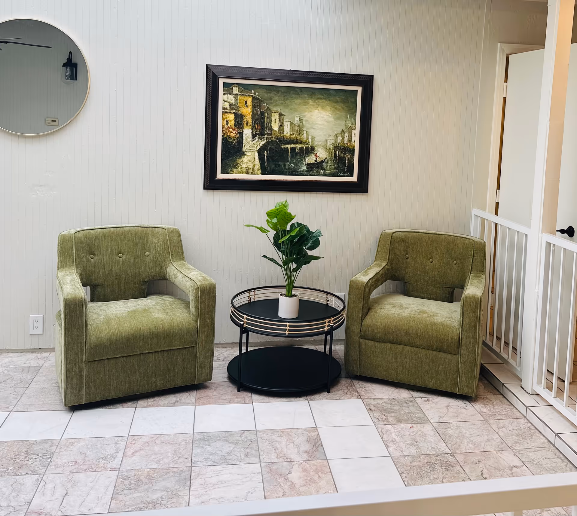 Two green armchairs flank a round table with a plant in a waiting lounge.