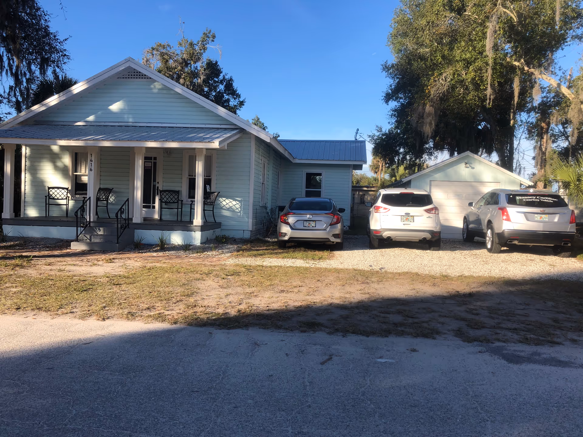 Front view of a light blue senior living facility with parked cars in a gravel driveway.