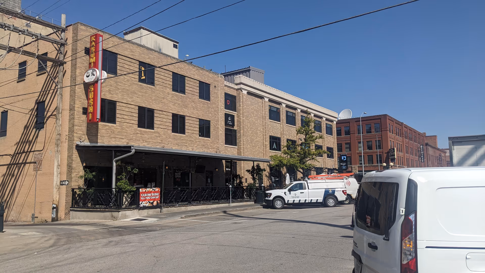 Exterior brick building along a city street with a covered patio and parked vans.