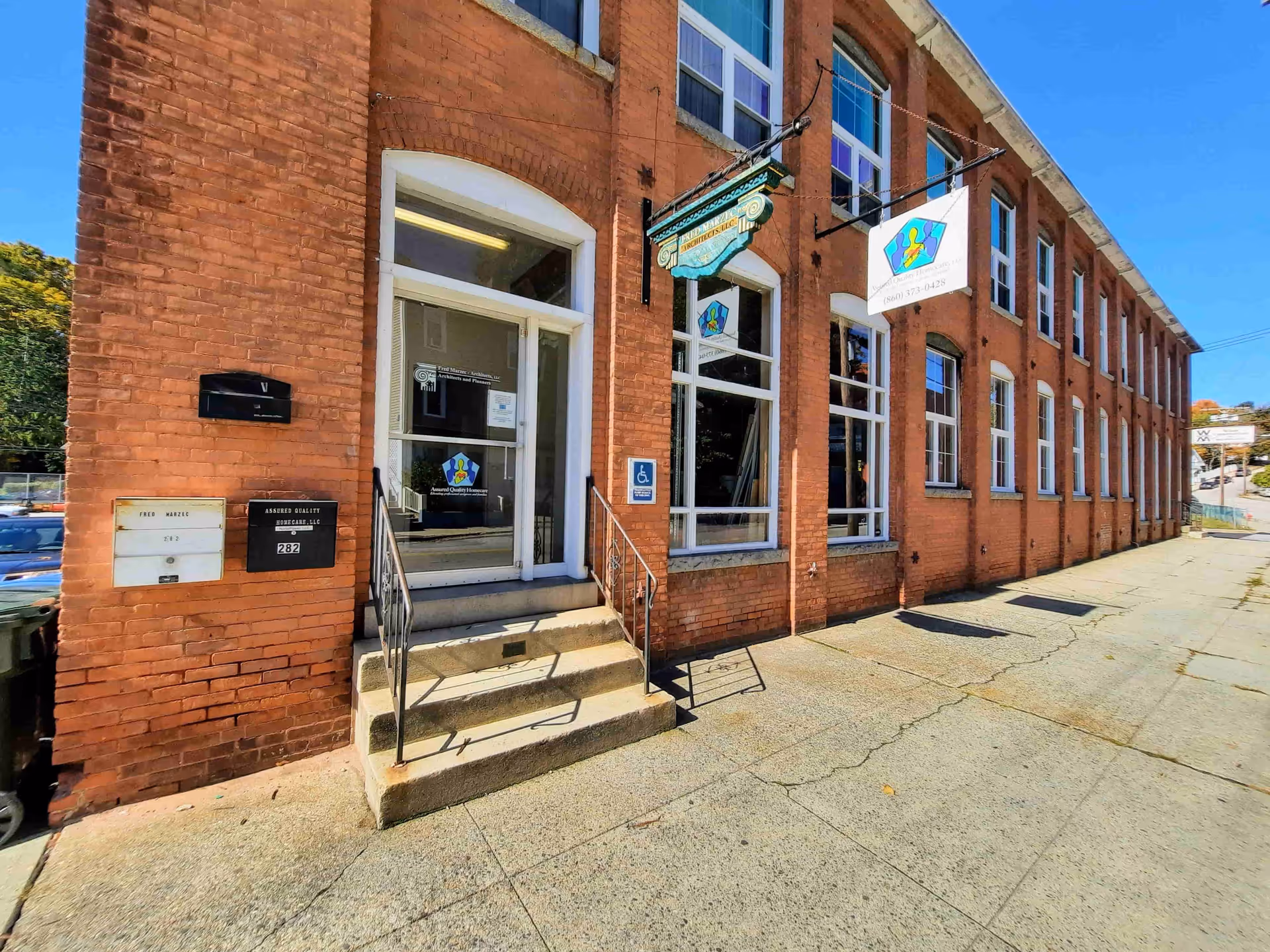 Brick building exterior with entrance stairs, large windows, and several signs.