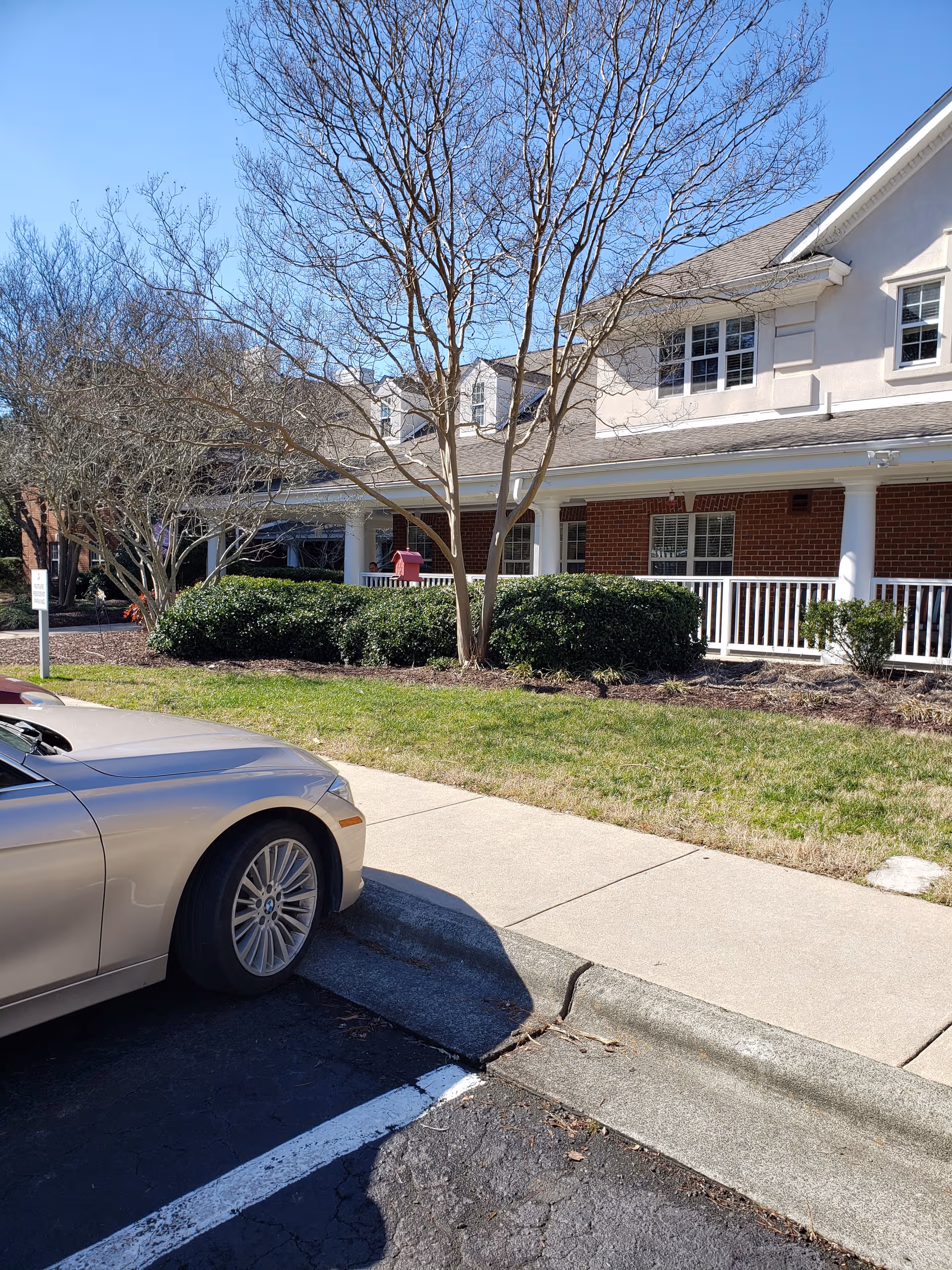 Exterior view of Brookdale Chapel Hill building with trees, shrubs, and a parked car.