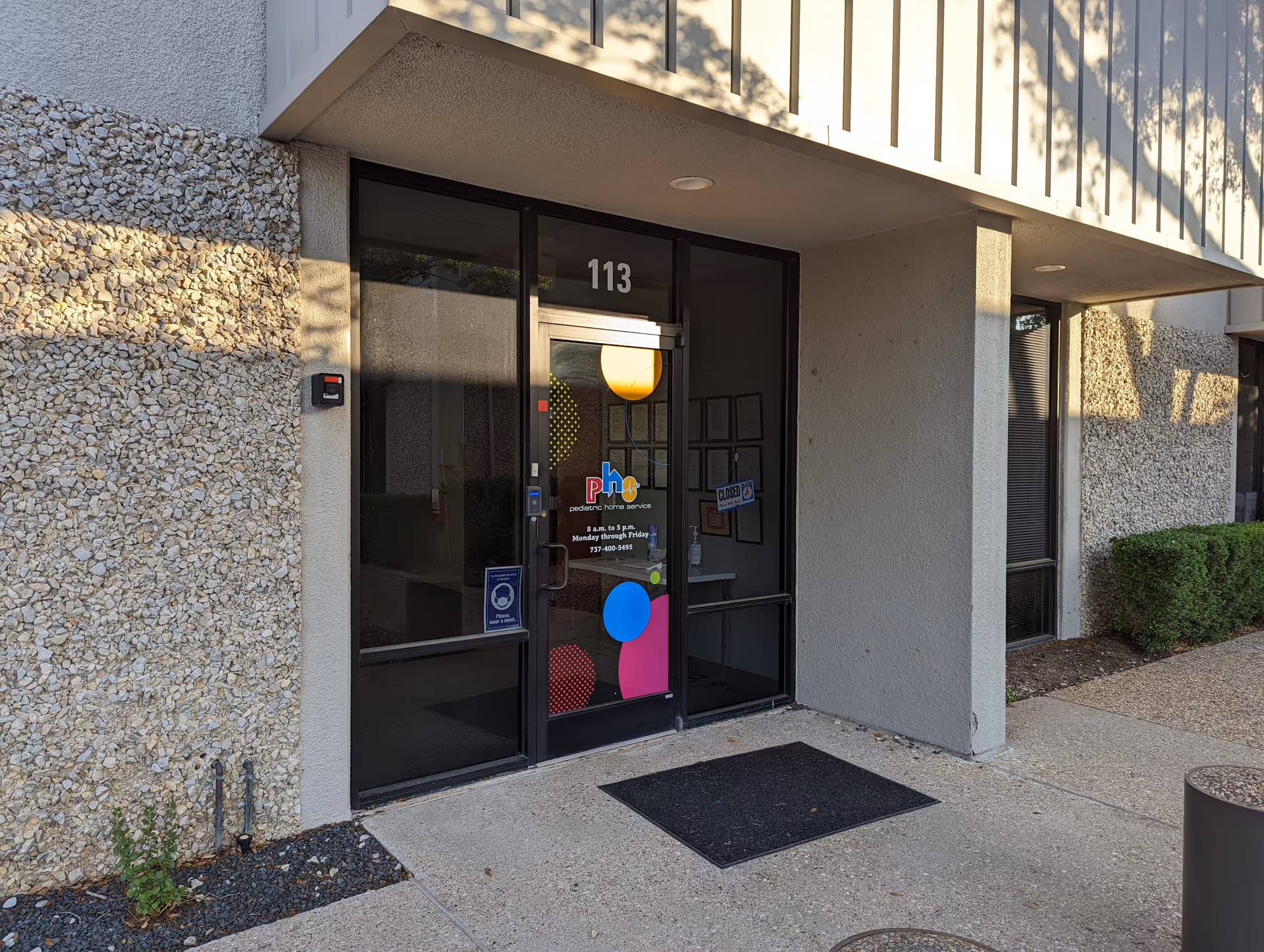Exterior building entrance with glass doors, pebble-textured walls, and the number 113.