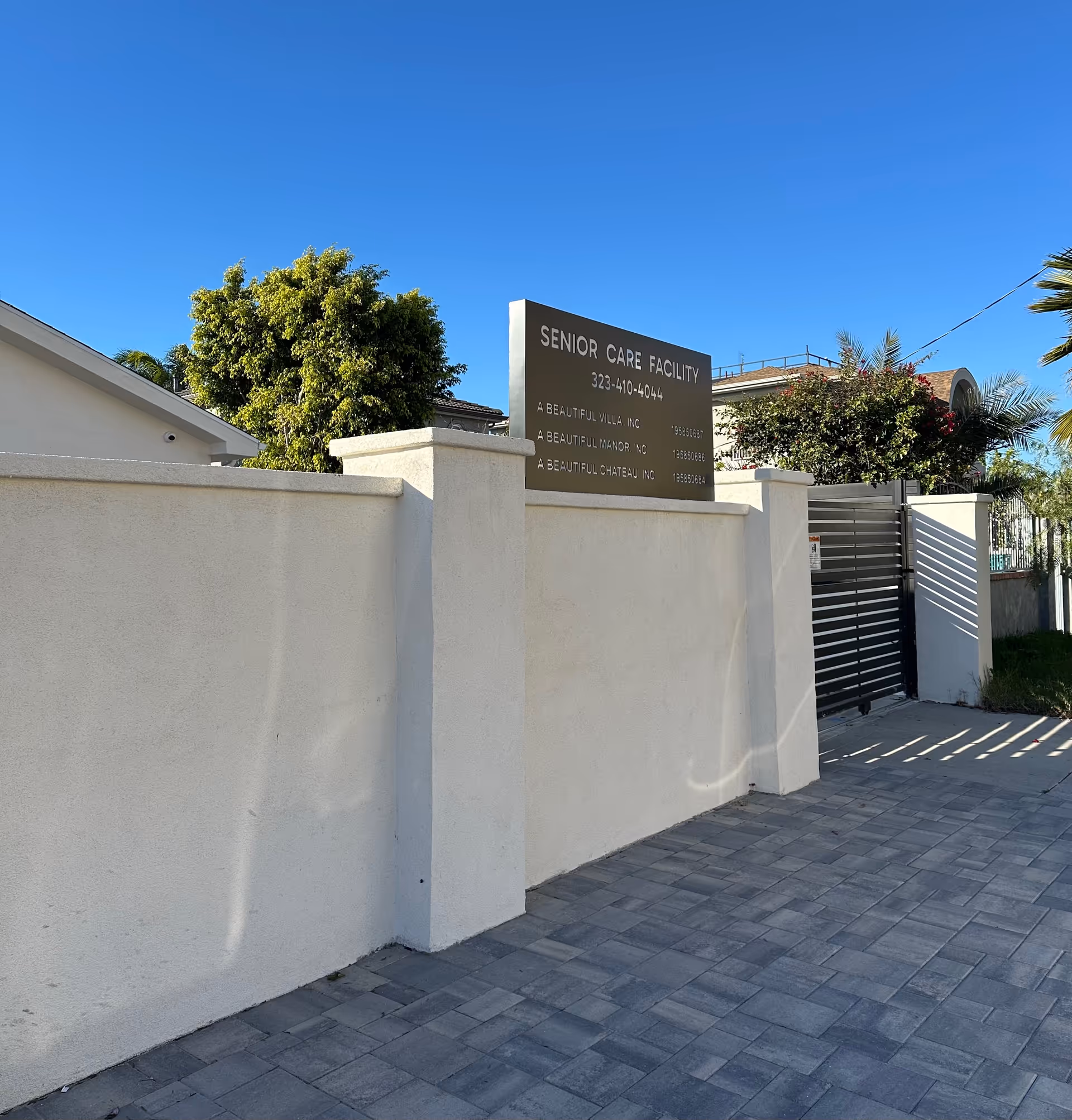 White exterior wall with a dark senior care facility sign and a gated entrance.