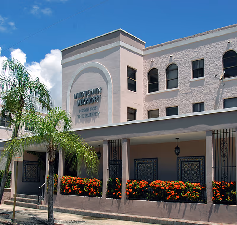 Exterior view of Midtown Manor senior living building with arches, palm trees, and flowers.