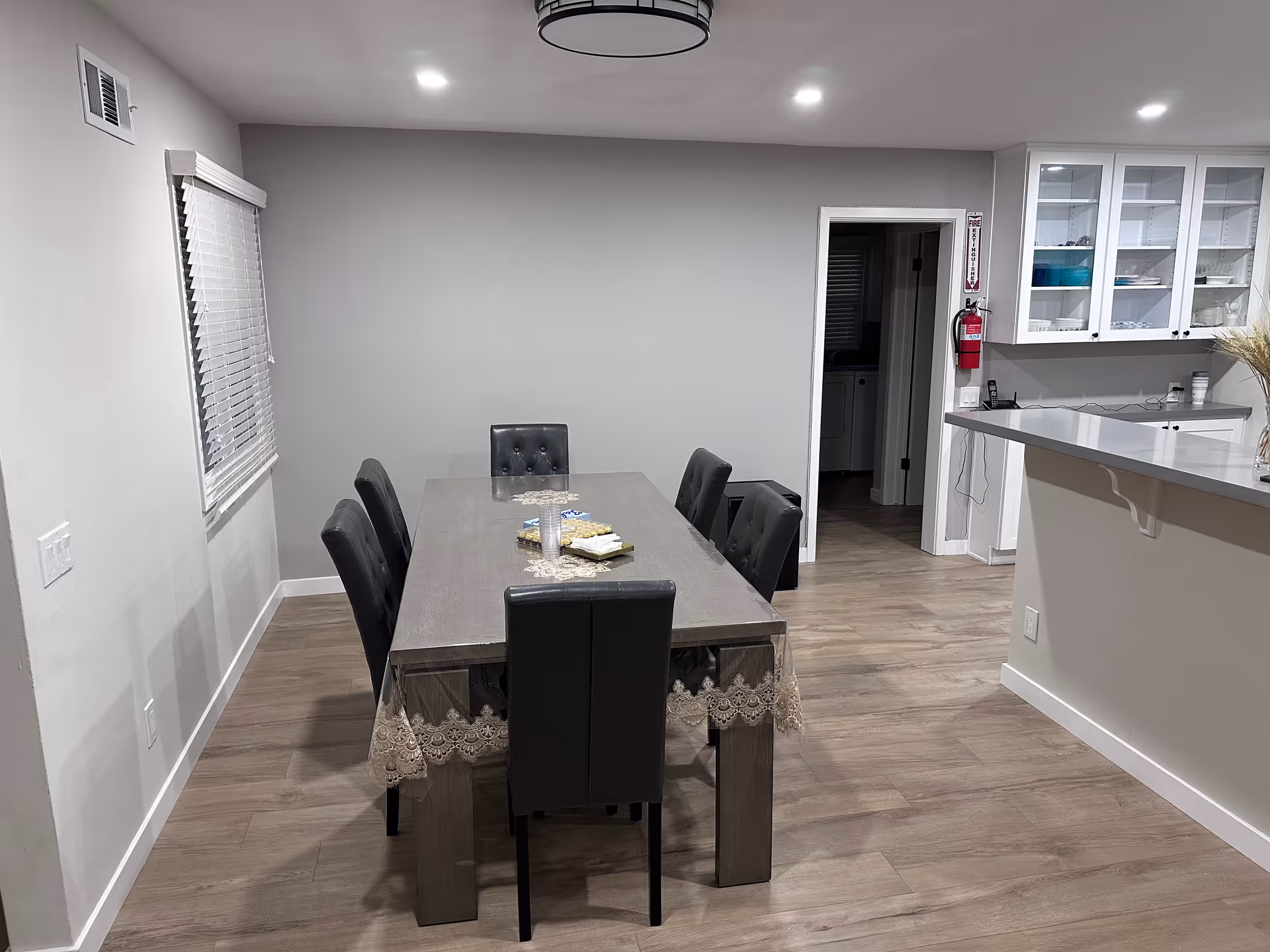 A communal dining table with six black upholstered chairs in a bright dining area.