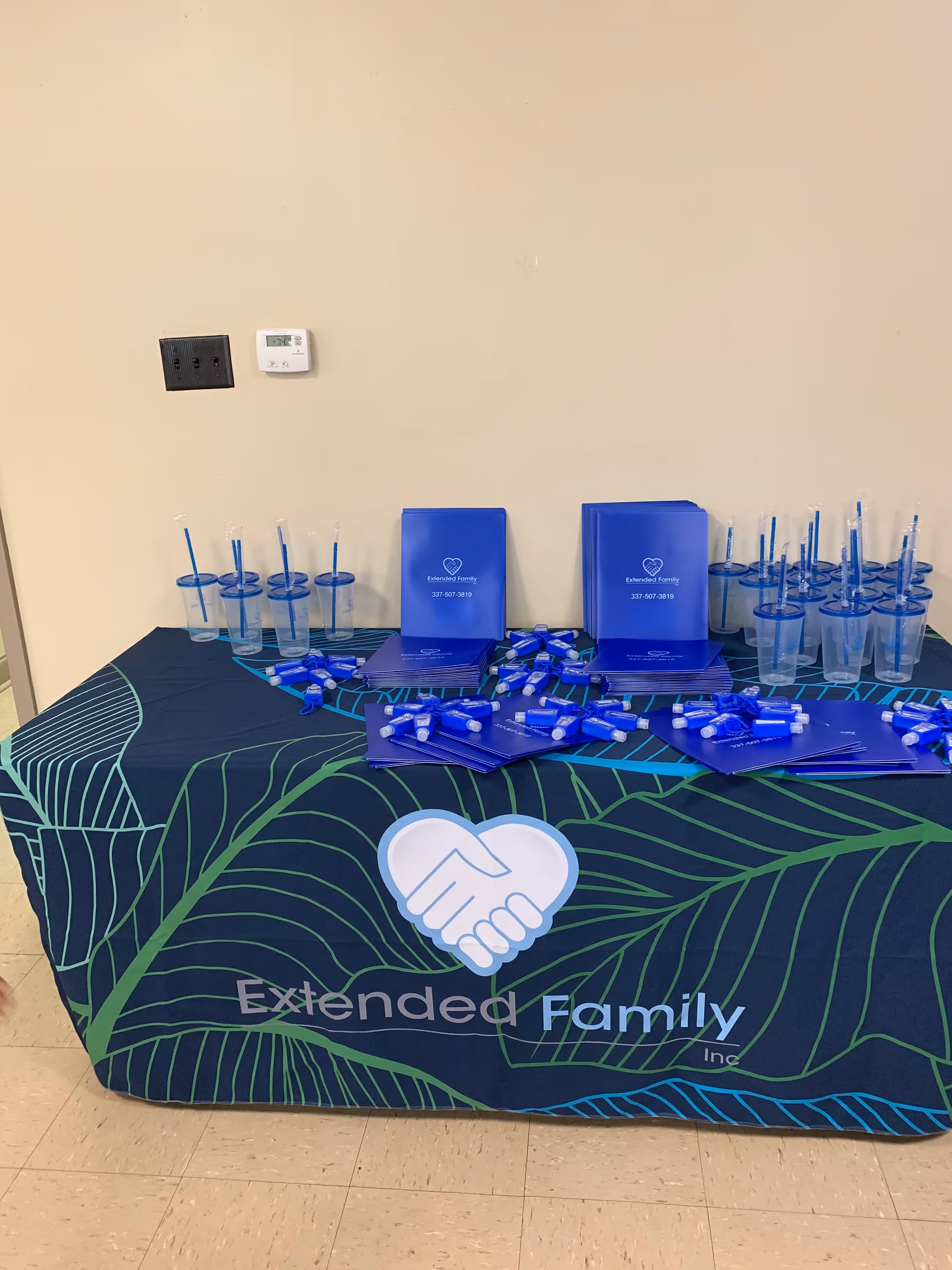 Promotional table with blue brochures, pens, and cups for Extended Family, Inc. indoors.