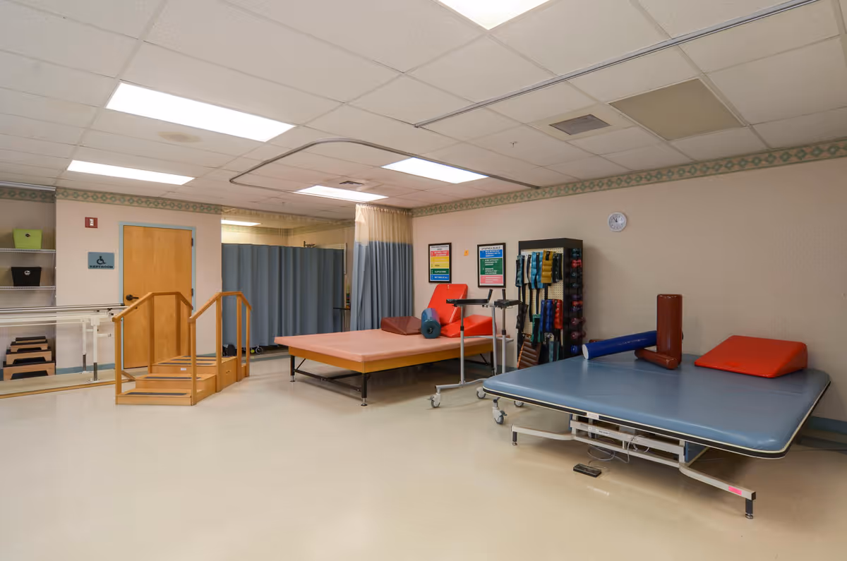 Rehabilitation room with mats, parallel bars, and exercise equipment inside a senior care facility.