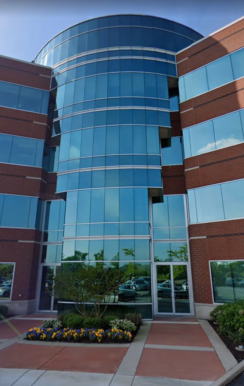 Modern glass-front building with curved glass tower and brick accents.