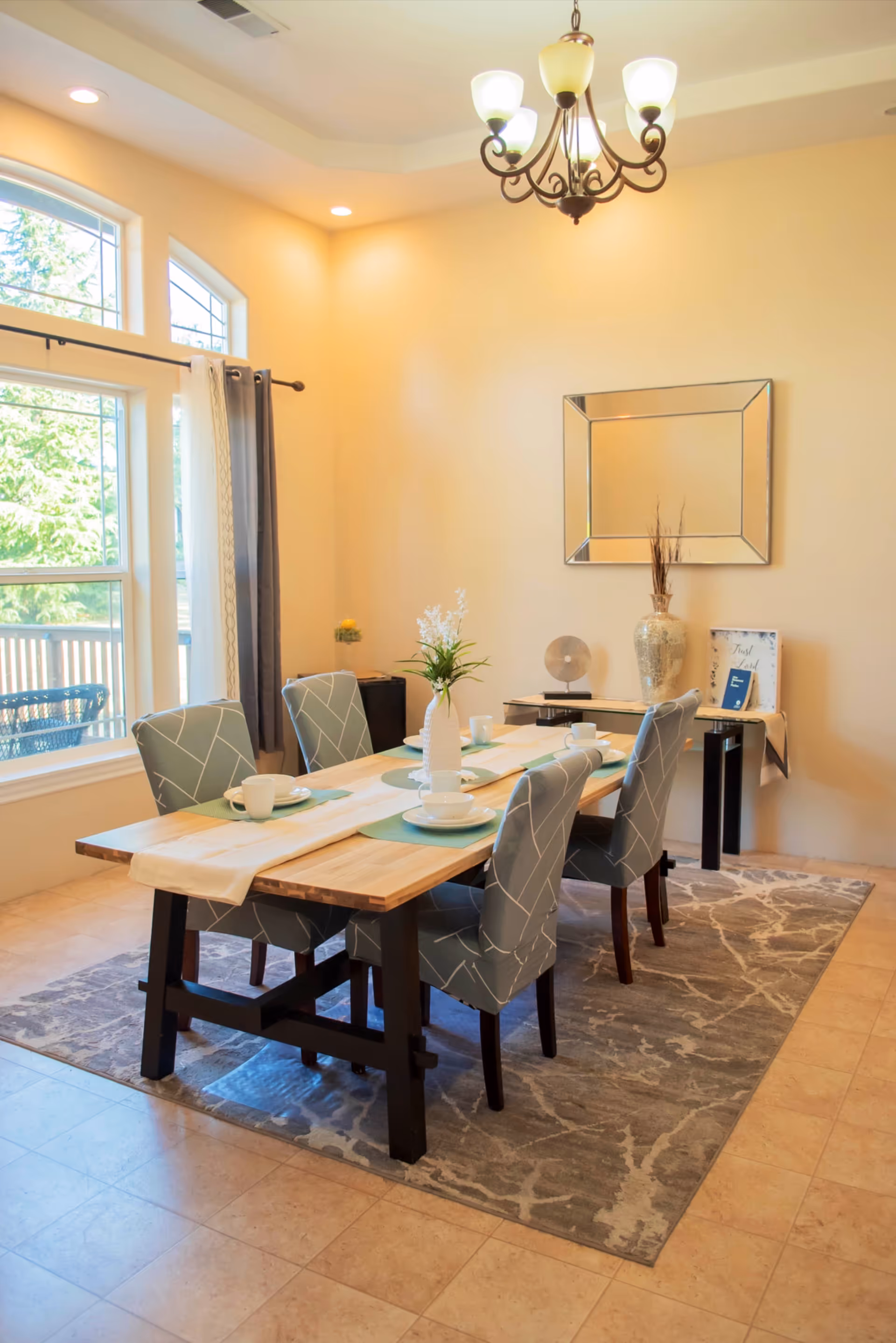 Dining room with a wooden table set for meals, patterned chairs, chandelier, and decorative wall mirror.