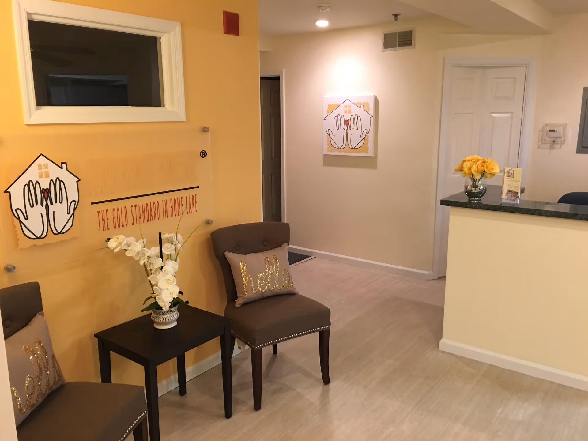 Lobby seating area with two chairs, a small table, wall art, reception desk, and flowers.