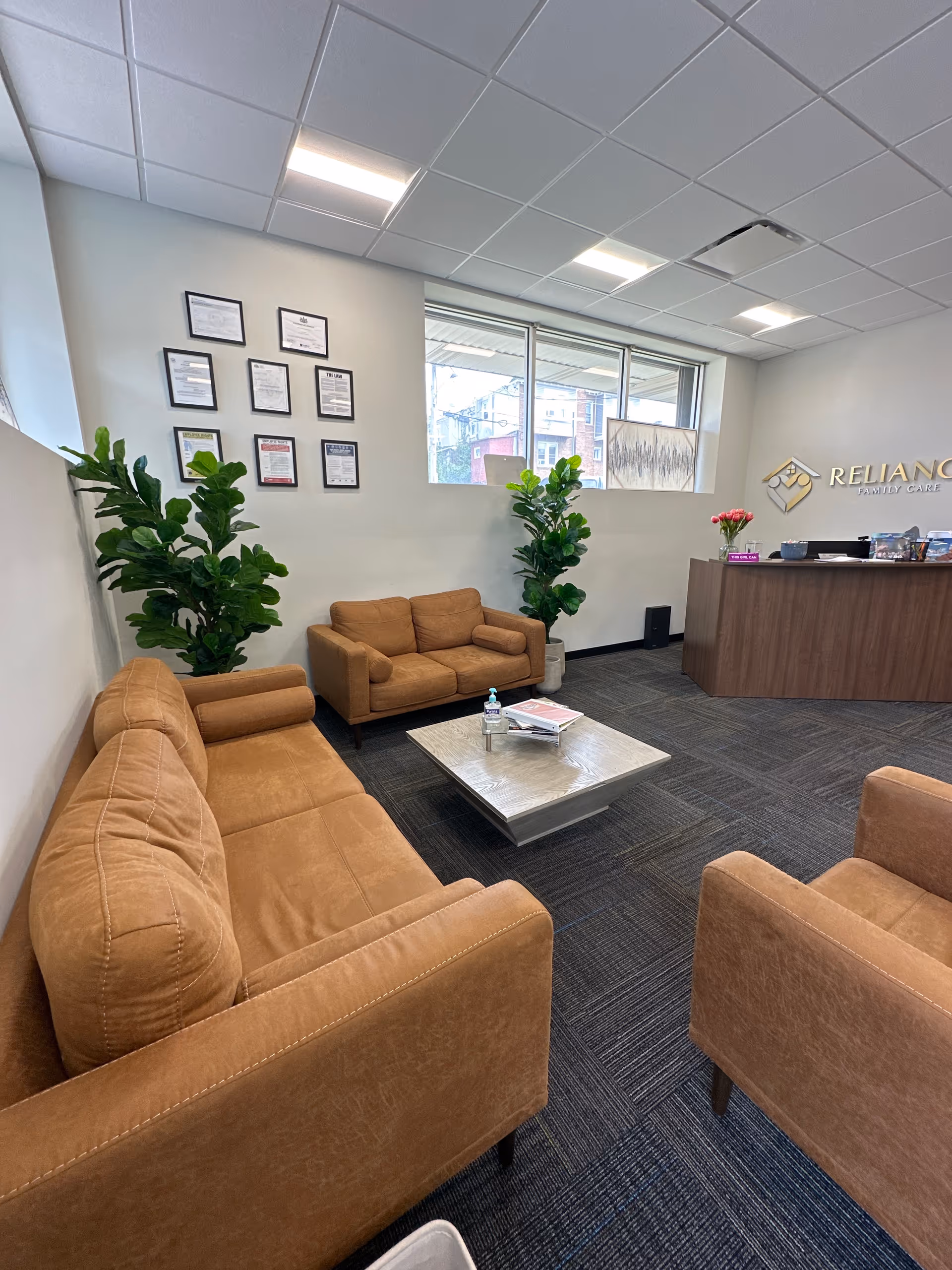 Lobby seating area with brown couches, plants, and a reception desk at Reliance Family Care