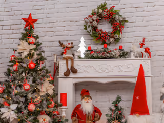 A festive Christmas tree stands beside a decorated mantel with a wreath indoors.