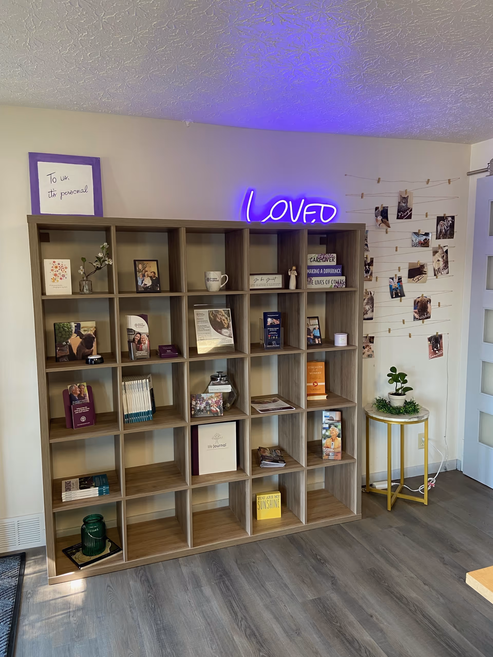Wooden cubby shelf filled with books and photos, purple neon 'Love' sign on wall.