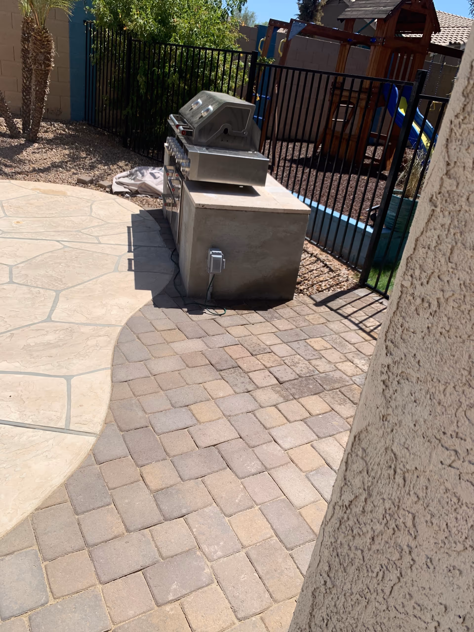 Outdoor patio with built-in grill, stone pavers, and a fenced playground.