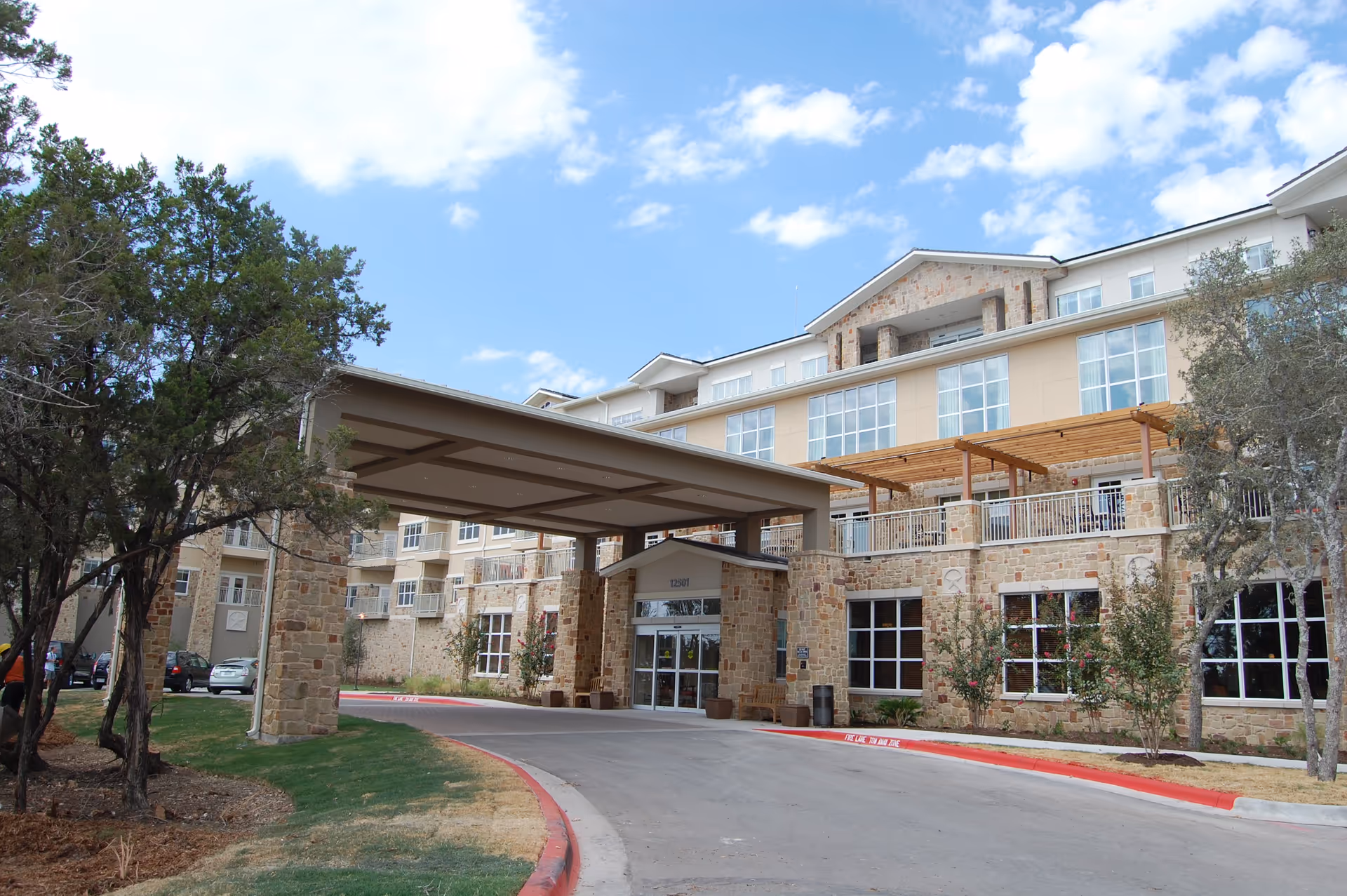 Stone-faced senior living building with a covered drop-off entrance and clear driveway.