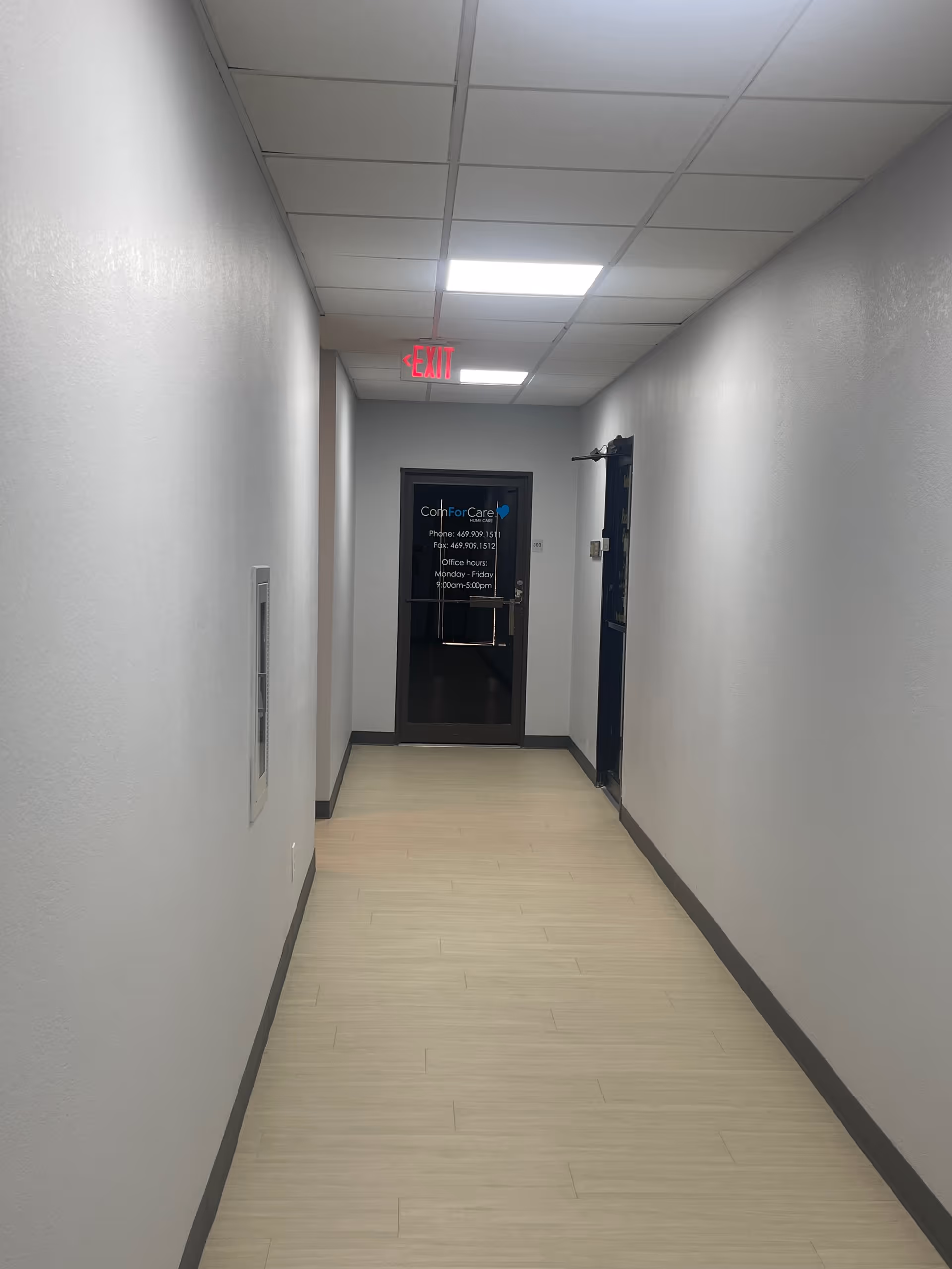 Long empty hallway inside a facility with a door at the end and exit sign