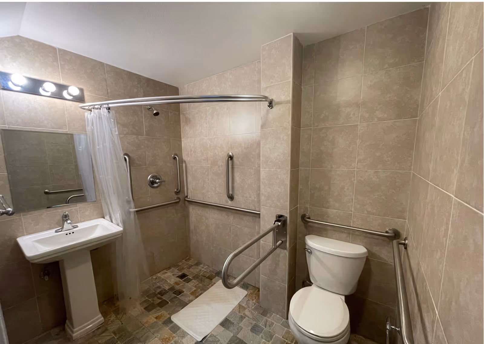 Accessible bathroom with shower stall, grab bars, sink, and toilet.
