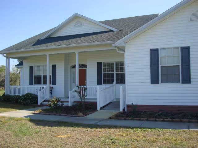 White single-story building with a front porch, columns, and landscaped entrance.