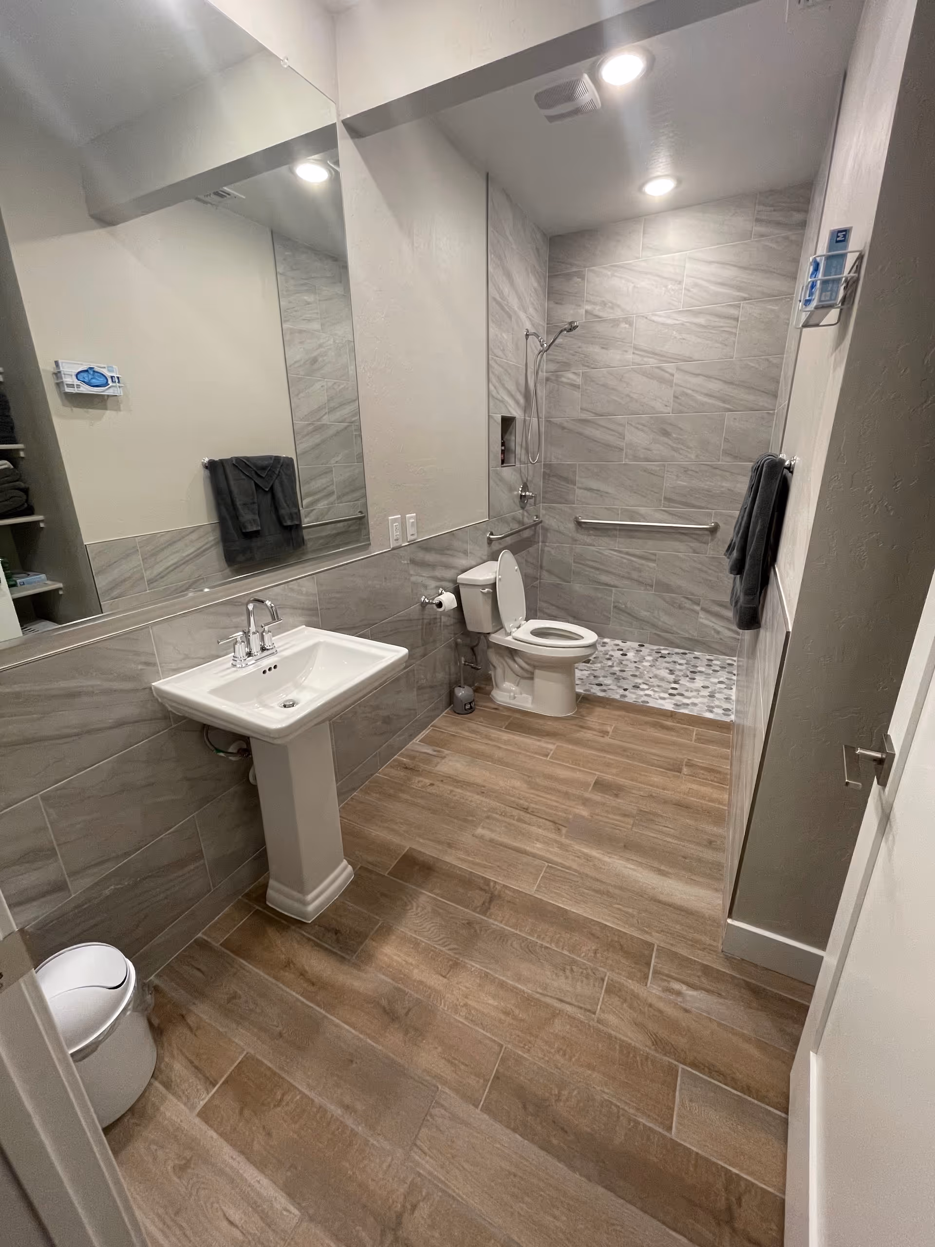 Accessible bathroom with pedestal sink, toilet, shower, and grab bars in a senior facility.