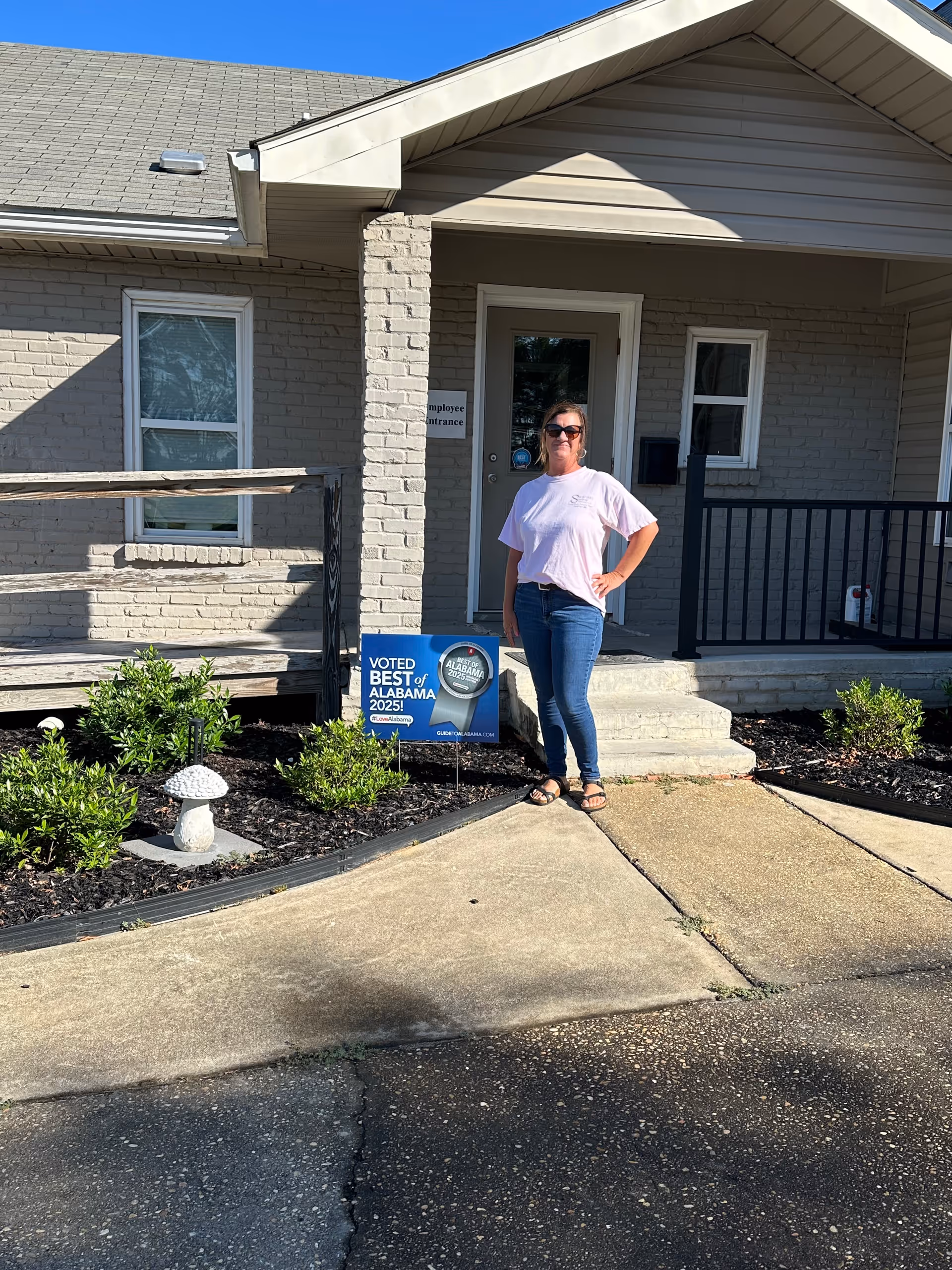 A woman stands outside a facility entrance beside a Best of Alabama sign.