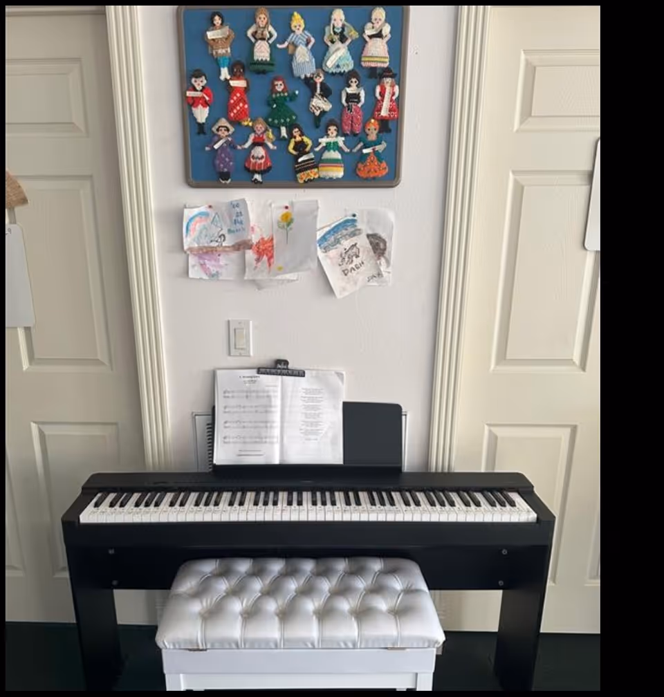 Black digital piano with sheet music, white tufted bench, and colorful wall drawings.