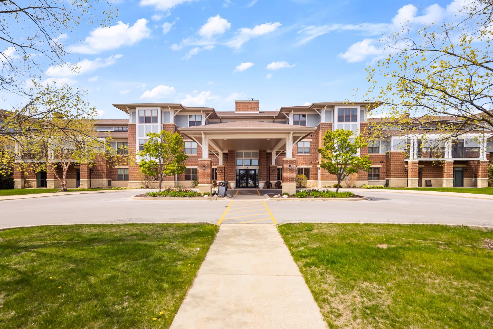 Front view of a brick senior living facility with a covered entrance and trees.