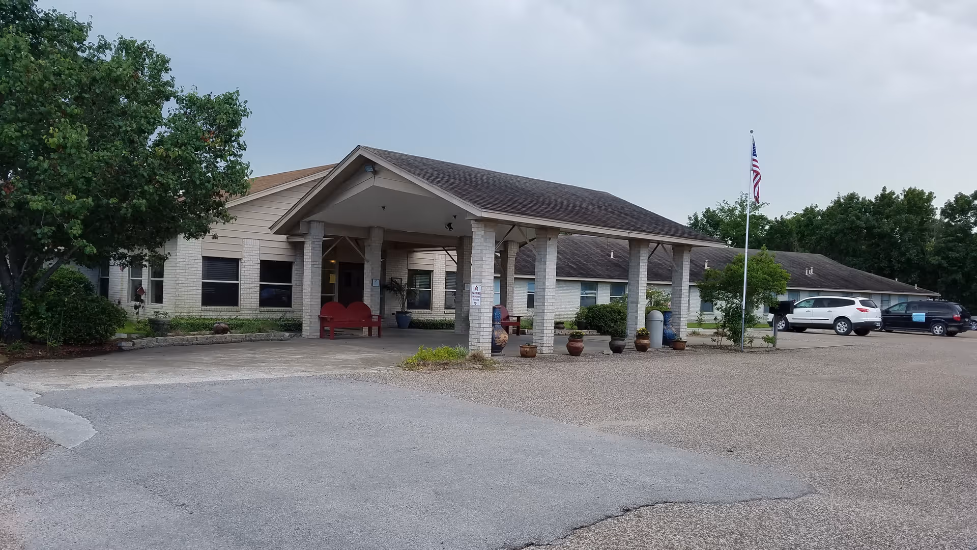 Exterior view of Riverwood Healthcare facility with a covered entrance, parked cars, and flag.