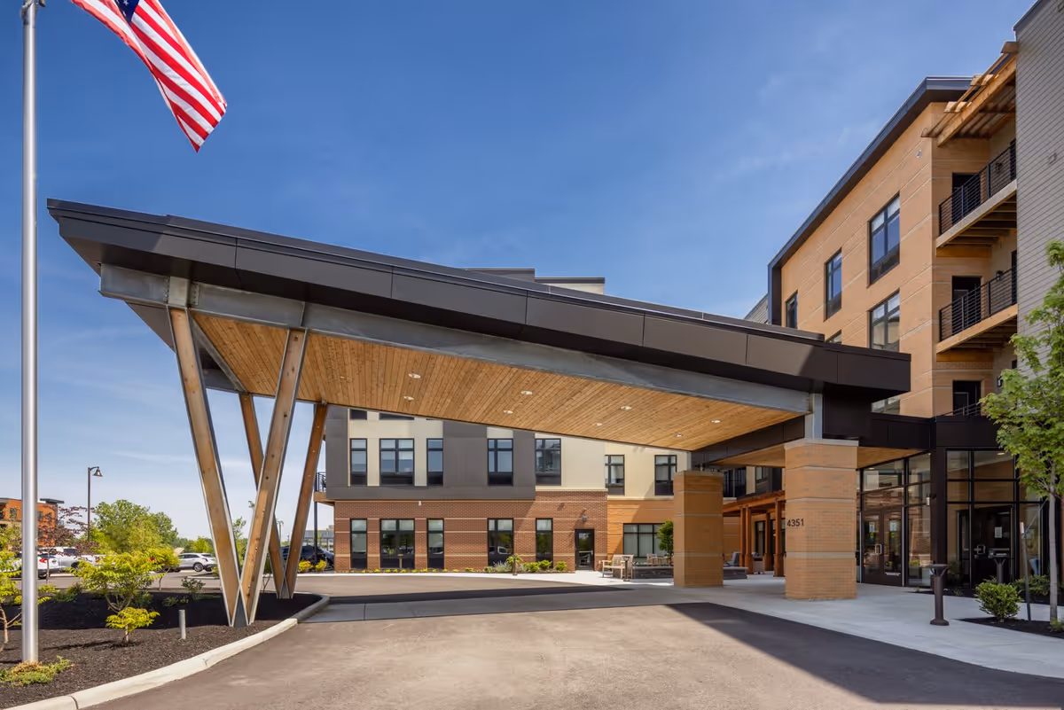 Covered entrance with a large angled canopy and an American flag in front of a multi-story senior living building.