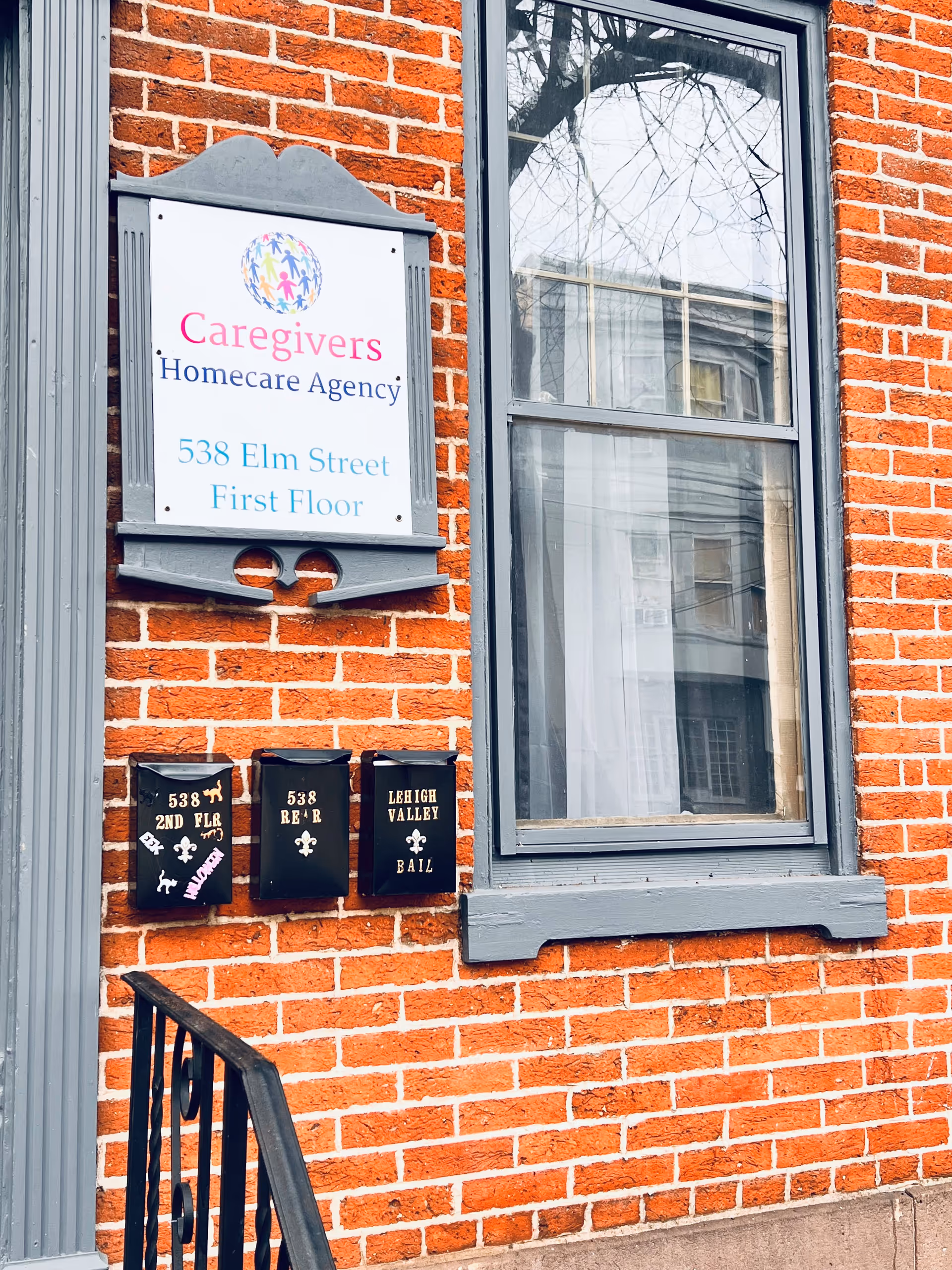 Brick building exterior showing a Caregivers Homecare Agency sign, a window, and three mailboxes.