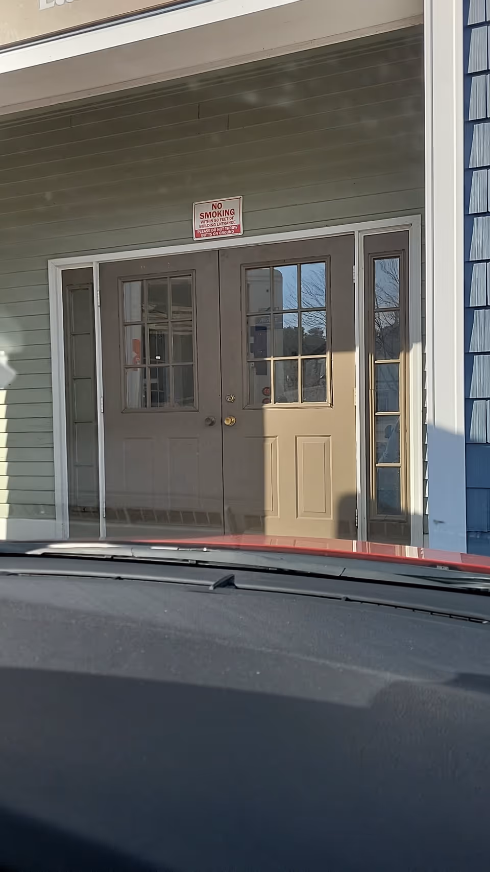 Front entrance doors of a building with a No Smoking sign above, viewed from inside car.
