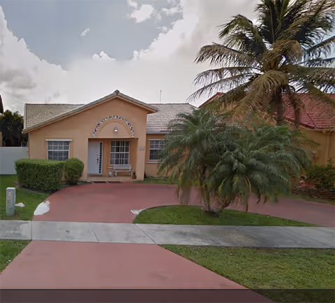 Single-story peach-colored facility with curved driveway, palm trees, and a front entrance.